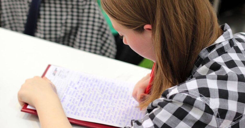 A young student writing in a notebook during a study session indoors.