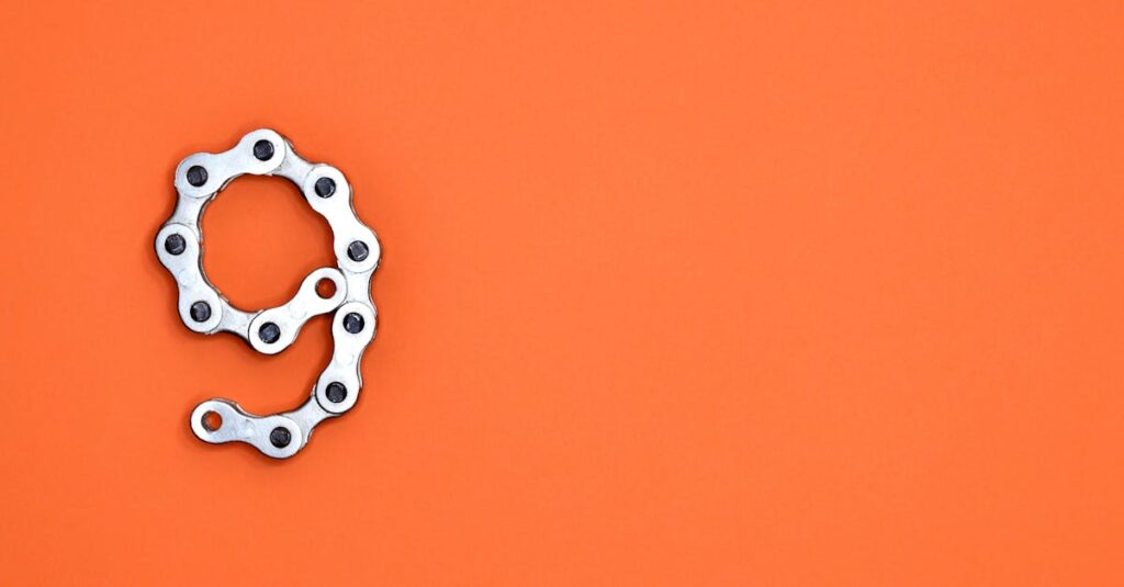 A metal chain shaped like the number nine against a vibrant orange background with copy space.