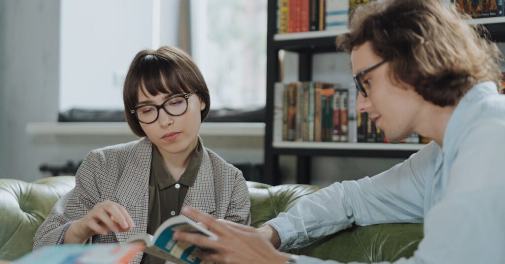 Two young adults reading and discussing in a cozy library space, sitting on a green sofa.