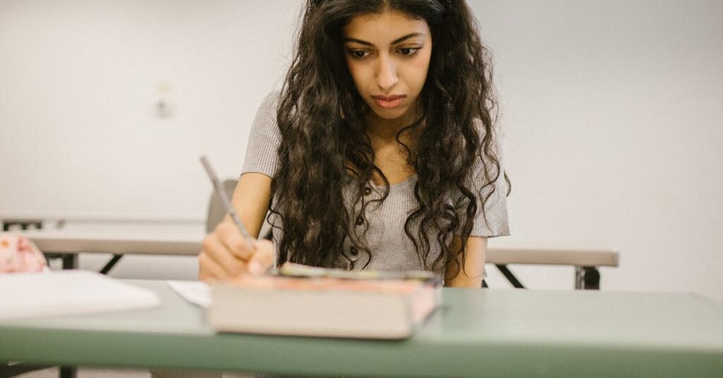 Focused college student writing notes with open book in classroom setting.