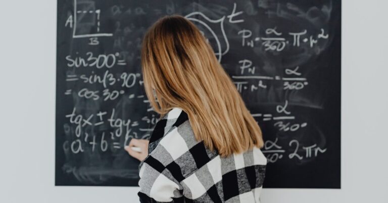 Teenager writing mathematical formulas on a blackboard in a classroom setting.