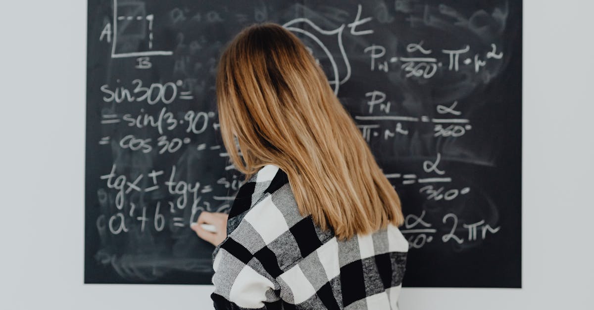 Teenager writing mathematical formulas on a blackboard in a classroom setting.